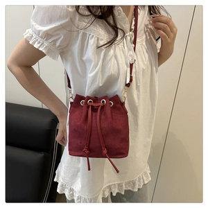 Detail of burgundy suede bucket bag with drawstring closure and golden eyelets