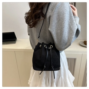 Side view of a black drawstring bucket bag worn by a model in a minimalist home setting