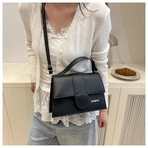 Detalle de bolso negro cruzado con logo metálico dorado y costuras verticales