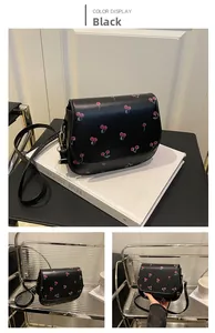 Detail view of black saddle bag with cherry print, smooth leather and metal hardware