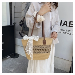 Detail of woven straw tote bag with large white lace bow and brown leather shoulder strap