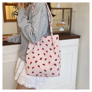 Dettaglio della borsa tote in velluto rosa con stampa fragole indossata sulla spalla