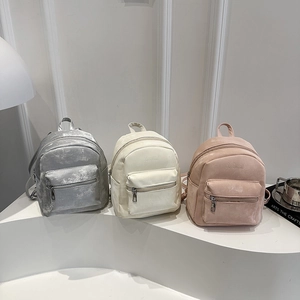 Three minimalist mini backpacks in silver, beige, and pink colors on a white pedestal