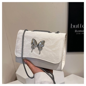 Gros plan du sac en cuir plissé blanc avec breloque papillon et bandoulière chaîne