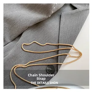 Détail d'une bandoulière chaîne serpent dorée sur le tissu d'un blazer gris chic
