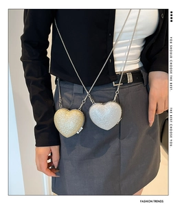 Detail of heart-shaped mini chain bags in gold and silver glitter finish on model