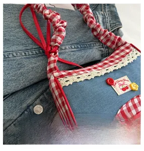 Detail of canvas handbag featuring gingham handles, lace trim, and cherry embroidery patch