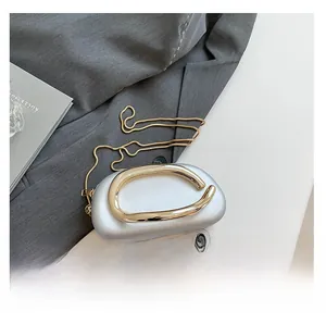 Détail d'une pochette argentée avec poignée dorée à côté d'un téléphone pour l'échelle
