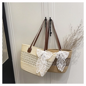 Detail of woven straw tote bag featuring decorative white lace bow and brown leather straps