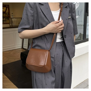 Brown leather saddle bag styled on a grey suit with a chic urban outdoor background