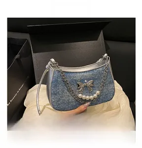 Detail of blue glitter handbag featuring silver butterfly and pearl chain on silk fabric