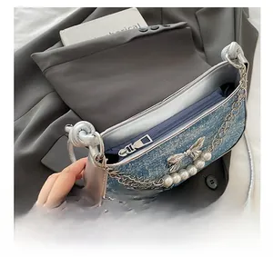 Detail of blue denim shoulder bag featuring silver bow, pearl charms and smooth zipper
