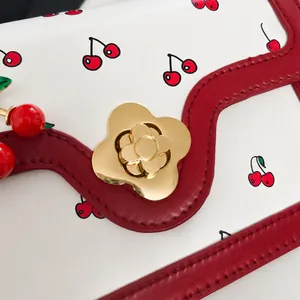 Gros plan du fermoir fleur dorée sur le sac à main blanc au motif cerise frais