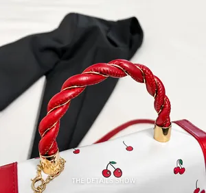 Détail de la poignée torsadée rouge avec chaîne dorée sur sac à cerises