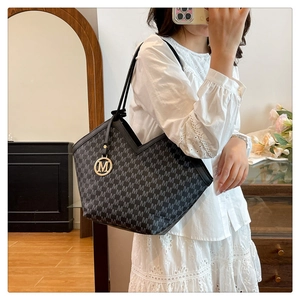 Gedetailleerde close-up van de zwarte shopper met gouden M-monogram en metalen hanger