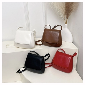 Four vintage saddle bags in white, brown, black and red colors on a white display stand
