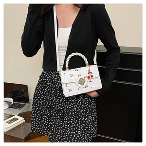 Détail du sac à main blanc à motif cerises avec fermoir fleur et anse tressée