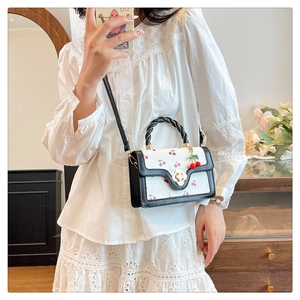 Détail du mini sac à bandoulière blanc avec motifs cerises et fermoir floral doré sur modèle