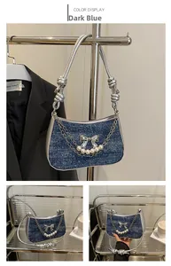 Detailed close-up of dark blue denim underarm bag with silver bow and pearl chain straps
