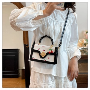 Détail du sac à bandoulière blanc à motif cerises avec poignée tressée et boucle dorée