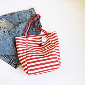Vista piatta di una borsa tote in tela a righe rosse e bianche con un ciondolo a pompon