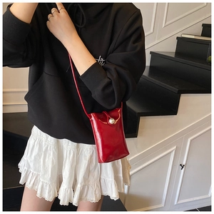 Detalle de un mini bolso rojo de charol para móvil con una elegante hebilla de perla