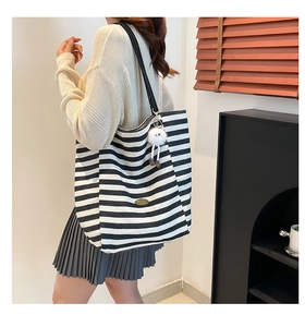 Detalle del bolso tote de lona a rayas con asas negras y colgante de peluche blanco