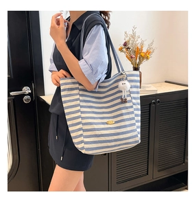 Dettaglio borsa tote in tela a righe blu con tracolla e ciondolo in peluche bianco