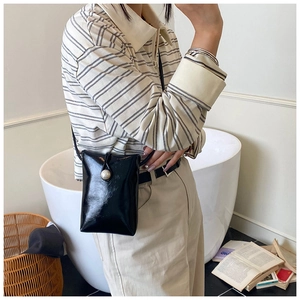 Detalle de un bolso bandolera de charol negro con hebilla de perla blanca en una modelo