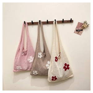 Three hollow knit tote bags with floral patterns hanging on a wooden wall hook