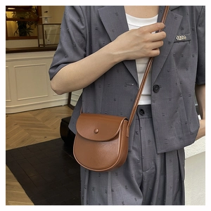 Close-up of brown semi-circular leather crossbody bag with flap and decorative button
