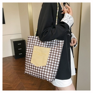 Detail of checkered canvas tote bag with woven straps and front pocket on casual model