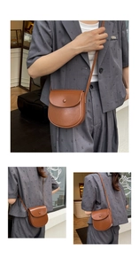 Detail of a minimalist brown saddle crossbody bag in smooth matte finish on a model