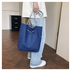 Detail of blue canvas tote bag with multi-color striped handles and checkered lining