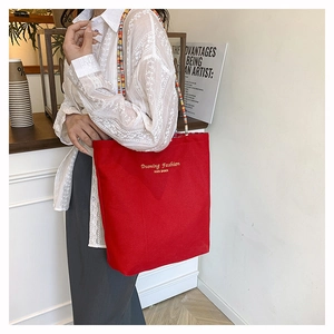 Dettaglio della borsa tote in tela rossa con tracolla di perline boho e scritte dorate