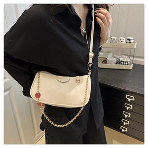 Detail of cream leather baguette bag with chic strawberry charm and gold chain strap