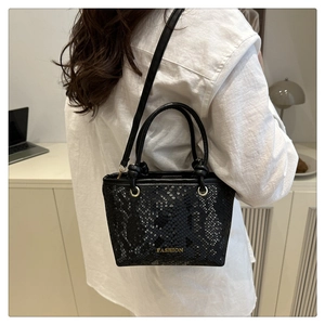 Détail du petit sac noir à texture serpent avec logo en métal et double poignée élégante