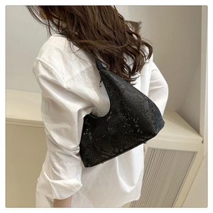 Dettaglio borsa sottobraccio nera motivo serpente con silhouette a mezzaluna su lino bianco