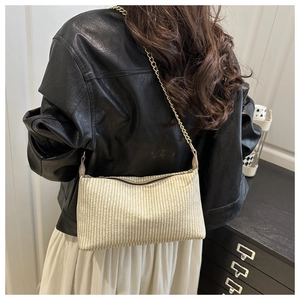 Close-up of beige woven texture with gold chain strap on a stylish underarm bag