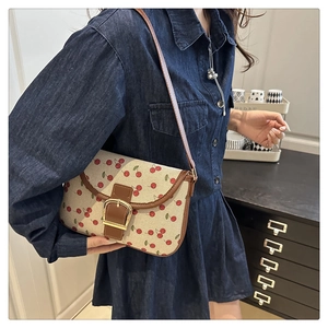 Detail of cherry print canvas bag with brown leather trim and large gold metal buckle