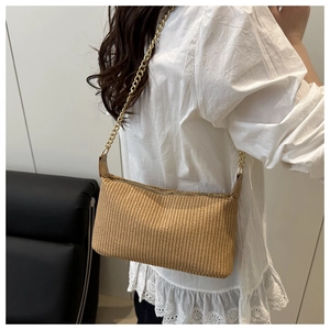 Detail of handwoven straw shoulder bag with vertical texture and gold chain strap