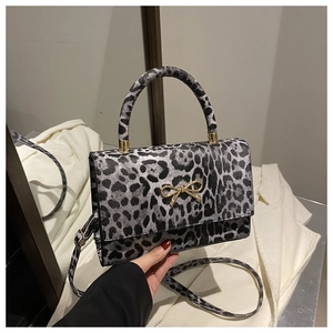 Detail einer Handtasche mit Leopardenmuster, goldener Schleife und Schultergurt