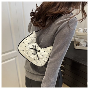 Détail du sac jacquard blanc avec nœuds noirs et pendentif en forme de cœur argenté