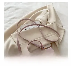 Detailed view of pink woven tweed handbag with gold buckle on a beige suit background