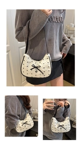 Detail of crescent shoulder bag with black bows and heart pendant on white texture