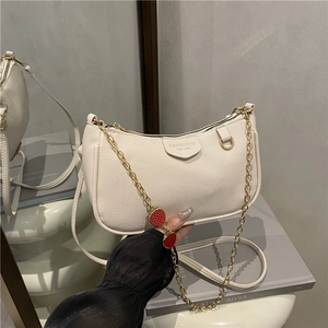Creamy crescent underarm bag with gold chain and red strawberry charms on white podium