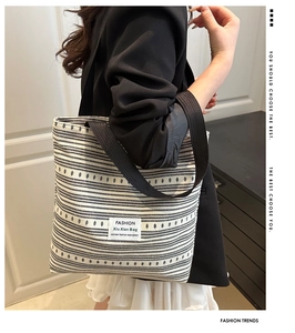 Gros plan d'un sac cabas en toile rayée avec anses noires tissées porté par un mannequin