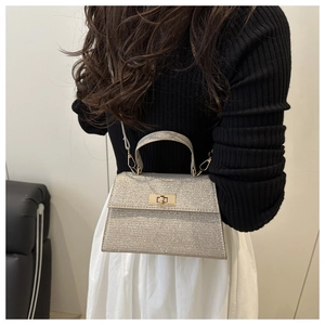 Detail of silver glitter trapezoid handbag with metal clasp held by a stylish model
