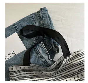 Détail montrant la sangle noire robuste fixée sur un sac cabas en denim rayé