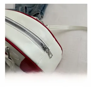 Détail de la fermeture éclair argentée et coutures sur un sac bandoulière rouge et blanc